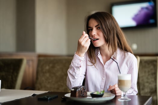 Young beautiful brunette woman sit in coffee shop cafe restaurant indoors and eat chocolate brownie dessert cake, fork near the mouth. photo