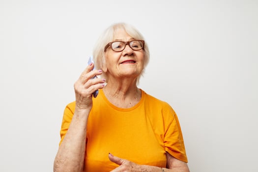 elderly woman in a yellow t-shirt posing communication by phone light background photo
