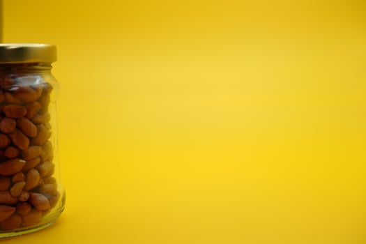 glass jar filled to the brim with shelled nuts. glass bottle filled with peanuts isolated on yellow background. photo