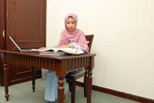 young Asian Malay muslim woman wearing headscarf at home office student sit at table computer read book file paper study work photo