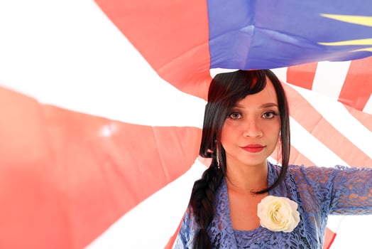 South east Asian Malay race ethnic origin woman wearing blue kebaya dress costume sharee multiracial community holding under Malaysian flag Jalur Gemilang on white background photo