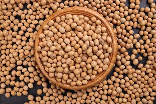 Soyabeans soya beans in wooden bowl flowing over black slate stone background copy text space flat lay top view photo