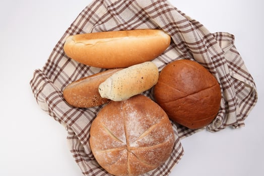 Freshly baked bread loaf bun roll round long mix verity wrapped in checkered kitchen fabric napkin towel over white background photo
