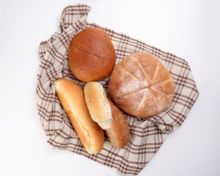 Freshly baked bread loaf bun roll round long mix verity wrapped in checkered kitchen fabric napkin towel over white background photo