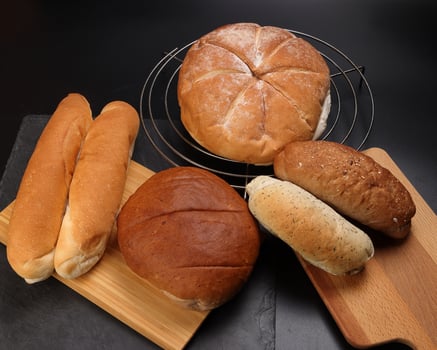 Freshly baked bread loaf bun roll round long mix verity on wooden board metal grill over black background photo