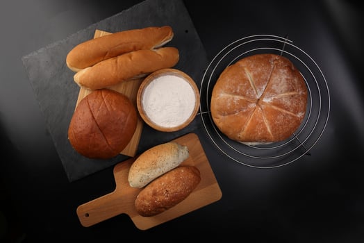 Freshly baked bread loaf bun roll round long mix verity flour in wooden bowl on wooden board metal grill over black background photo