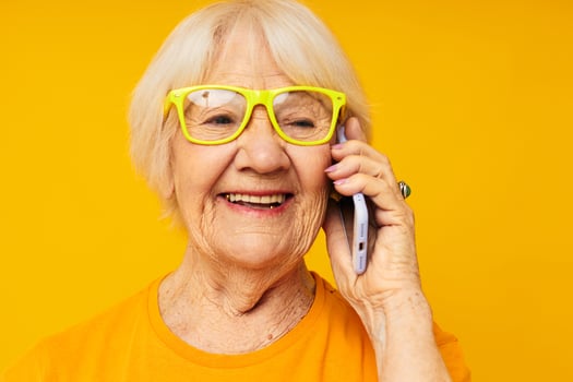 smiling elderly woman talking on the phone in yellow glasses isolated background photo