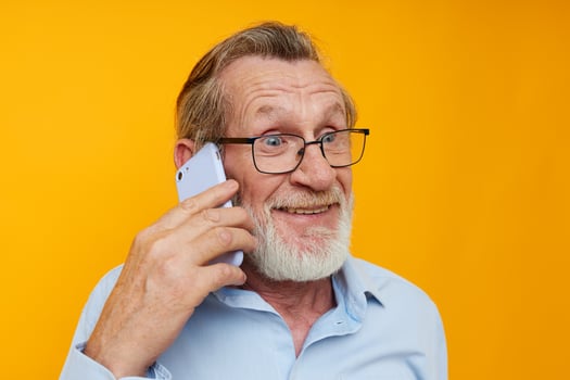 Portrait elderly man gray beard with glasses talking on the phone yellow background photo