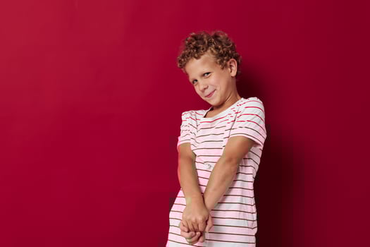 Cheerful boy in a striped T-shirt gestures with his hands red background photo