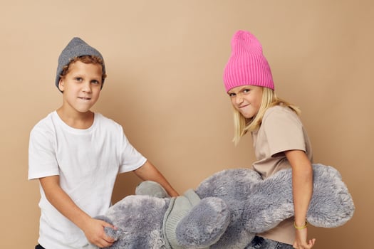 Photo of two children in multi-colored hats entertainment posing beige background