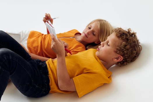 picture of positive boy and girl lie on the floor with notepads and pencils isolated background unaltered photo
