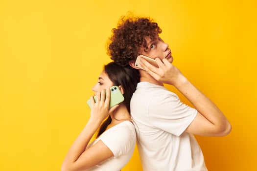 a guy and a girl stand with their backs to each other talking on the phone photo