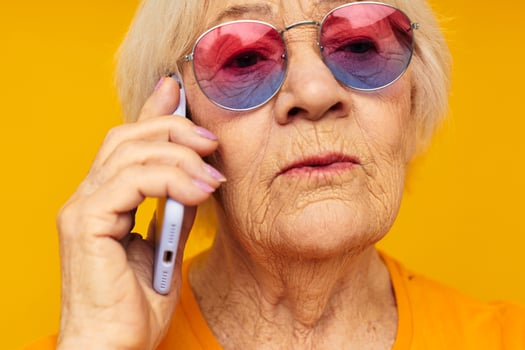 elderly woman talking on the phone in yellow glasses yellow background photo