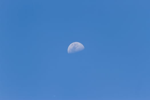 A horizontal shot of a half-moon visible during daylight in the blue sky photo