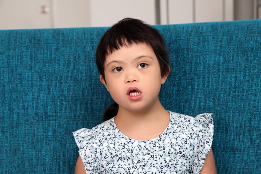 Southeast Asian small little girl child sitting on blue sofa look happy smile pose. She have down syndrome photo