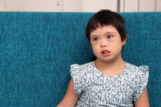 Southeast Asian small little girl child sitting on blue sofa look happy smile pose. She have down syndrome photo