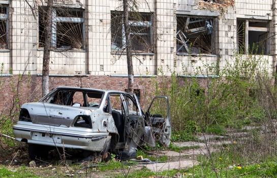 A broken Ukrainian civilian car, shot by artillery, stands in the courtyard of a destroyed house. War between Russia and Ukraine. The wreckage of an abandoned car. photo