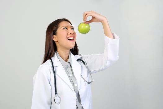 Young Asian female doctor wearing apron uniform tunic stethoscope holding pointing showing eating healthy green apple photo