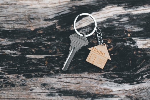 House key on a house shaped keychain resting on wooden floorboards concept for real estate renting property. House model and key in house door. Real estate agent offer house, property insurance. photo