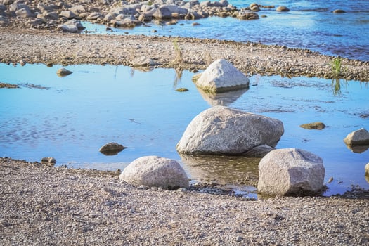 Close up of rocks on the river bank near blue water puddle on sunny day photo