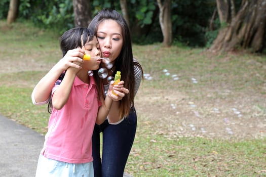 South East Asian young Chinese mother daughter parent child playing with soap bubbles relax activity outdoor park photo