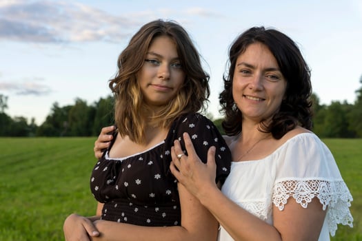 happy mom hugs her teenage daughter against a green field photo