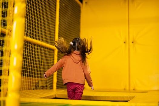 Little girl kid jumping on trampoline at yellow playground park. Child in motion during active entertaiments. photo