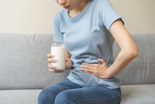 Pain, suffering asian young woman having a stomachache, abdominal pain or digestive, hand in holding belly after drink glass of milk. Lactose intolerance, allergy from dairy food, health care problem. photo