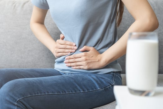 Pain, suffering asian young woman having a stomachache, abdominal pain or digestive, hand in holding belly after drink glass of milk. Lactose intolerance, allergy from dairy food, health care problem. photo
