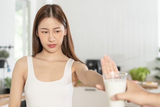 Allergy asian young woman, girl hand in deny, no or push out to avoid for drink milk at home, unhappy and bad stomach ache. Lactose intolerance and dairy food, health problem, belly suffer concept. photo