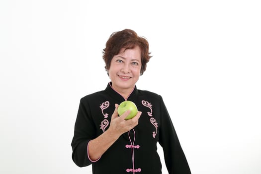 Elderly asian Chinese female wearing black tang samfu on white background holding green apple photo
