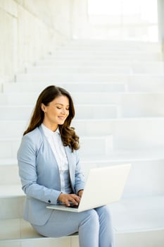 Young business woman sitting on the stairs on office hallway and working on laptop photo
