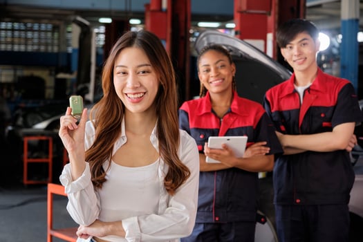 Young Asian female customer shows car key with automotive mechanic workers, happy smile in quality trust at maintenance garage, professional vehicle service center, fix check and repair auto industry. photo