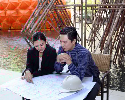 South East Asian young Malay Chinese man woman formalwear sit at table construction site study look plan blueprint photo