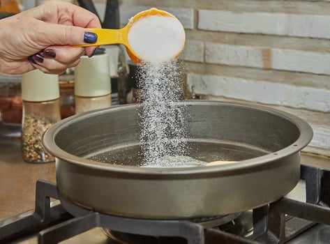 Chef pours sugar into frying pan with oil on gas stove photo
