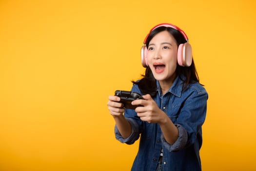 Portrait young asian woman with happy success smile wearing denim clothes holding joystick controller and playing video game. Fun and relax hobby entertainment lifestyle concept. photo