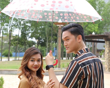 Young Asian Malay man woman outdoor green park walk talk discuss mingle under umbrella photo