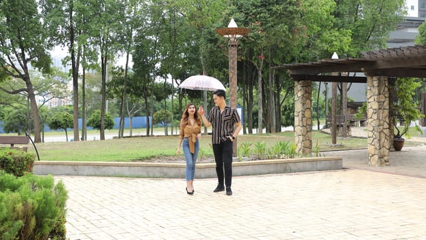 Young Asian Malay man woman outdoor green park walk talk discuss mingle under umbrella photo
