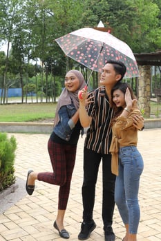 Young Asian Malay man woman outdoor green park walk talk discuss mingle under umbrella photo