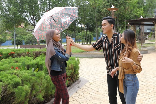 Young Asian Malay man woman outdoor green park walk talk discuss mingle under umbrella photo