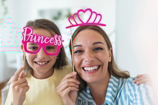 Funny family on a background of bright wall. Mother and her daughter girl with a paper accessories. Mom and child are holding paper crown on stick. photo