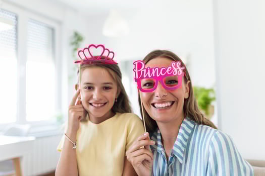 Funny family on a background of bright wall. Mother and her daughter girl with a paper accessories. Mom and child are holding paper crown on stick. photo
