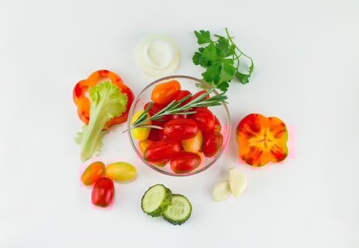 Cherry tomatoes in a salad bowl and chopped vegetables around, lettuce, peppers, cucumbers, onions. Top view, on a light background photo