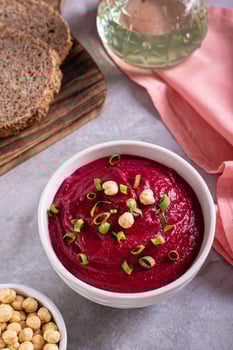 Bowl of vegetable beetroot hummus with chickpeas and herbs on the table vertical view photo