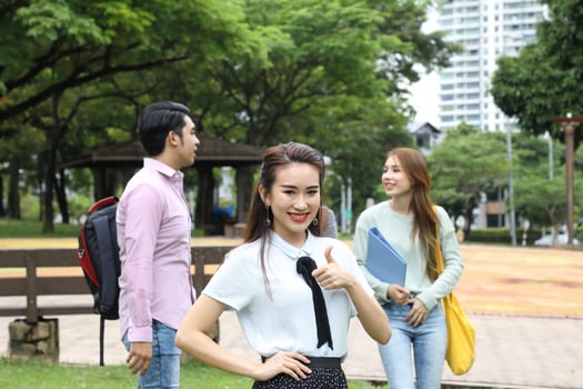 Young asian malay chinese man woman outdoor park walk stand study talk discuss point laptop file book backpack female look forward thumbs up photo