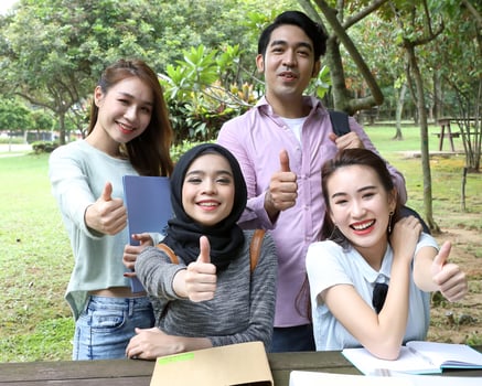Young asian malay chinese man woman outdoor on park bench table study talk discuss point laptop file book happy pose look forward thumbs up photo