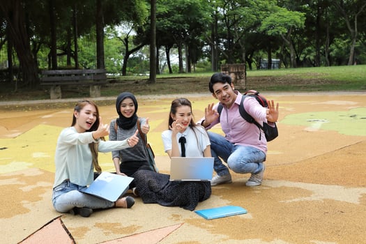 Young asian malay chinese man woman outdoor park sit on ground study talk discuss point laptop file book backpack mingle fun thumbs up photo