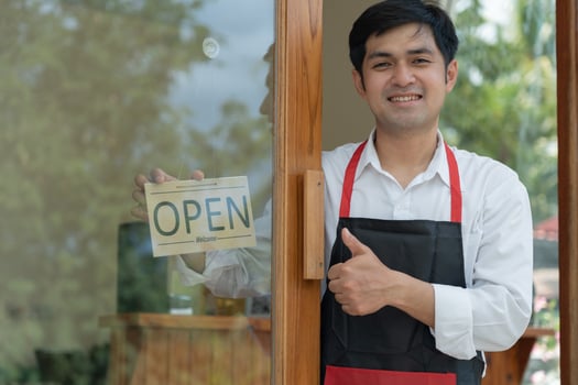 Business owner thumbs up to show his readiness to welcome customers. waitress man turning on open sign board on glass door in modern cafe coffee shop. New normal, small business, cafe, life style. photo