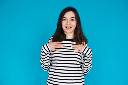 Portrait of a gorgeous, pretty, imposing girl in a striped pullover with her arms across her chest, isolated on a blue background photo