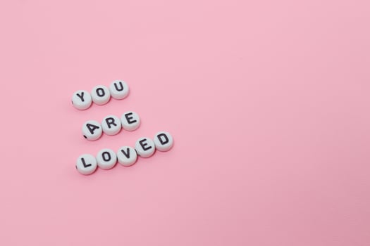Top view of you are loved quotes made out of beads on pink background. motivation and success concept photo